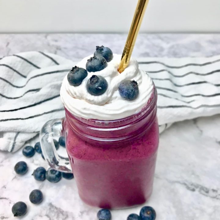 A blueberry milkshake topped with whipped cream and blueberries.